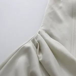 Gedetailleerde weergave van de elegante geplooide satijnen stof op een witte galajurk.