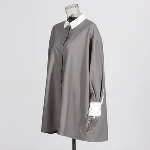 Detailweergave van een losse grijze tuniek met witte contrastkraag en manchetten.
