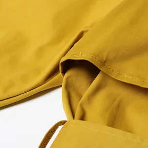 Macro view showing the fabric texture and tailoring of a mustard yellow trench coat.
