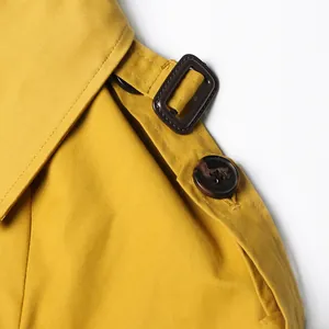 Close-up detail of a mustard yellow trench coat shoulder strap with button and buckle
