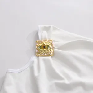 Detalle de la camiseta blanca con un original adorno de metal con forma de ojo.