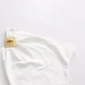 Detalle de un top blanco sin mangas con un adorno de ojo dorado decorado con perlas