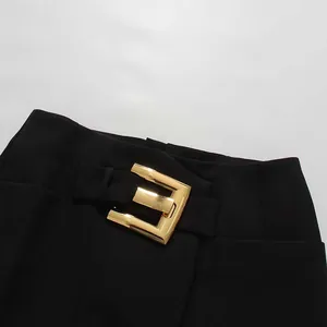 Close-up detail of a gold metal buckle on a black high-waisted elegant skirt.