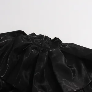 Detailed macro view of black ruffled collar blouse featuring metallic sheen fabric texture.