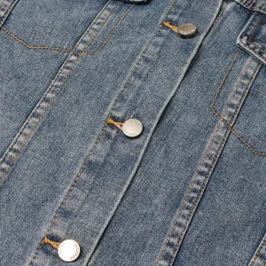 Nahaufnahme von Metallknöpfen und Kontrastnähten auf einer blau gewaschenen Jeansjacke