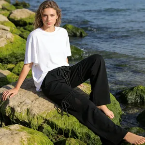Γυναίκα με μαύρο καλοκαιρινό παντελόνι με κορδόνι και λευκό μπλουζάκι στην ακροθαλασσιά