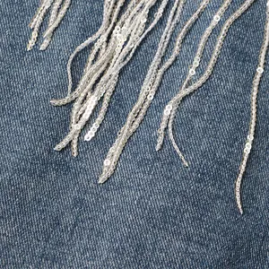 Detailansicht der schimmernden silbernen Paillettenfransen an blauer Jeansjacke.