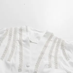 Detailed view of elegant white V-neck shirt with exquisite shoulder pearl bead embroidery