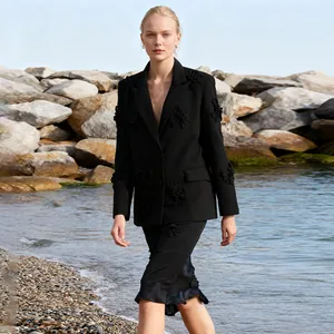 Elegante blazer nero stile francese con applicazioni floreali 3D sulla spiaggia.
