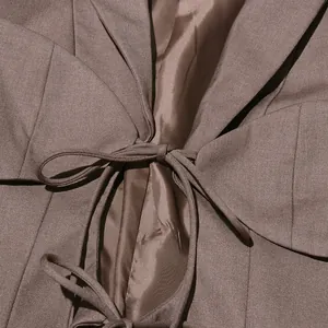 Dettaglio ravvicinato di un blazer slim taupe da donna con design stringato irregolare in vita