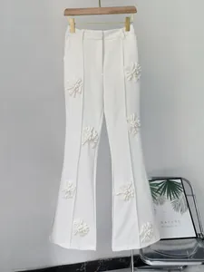 Dettaglio di pantaloni a zampa bianchi stile francese con eleganti applicazioni floreali 3D