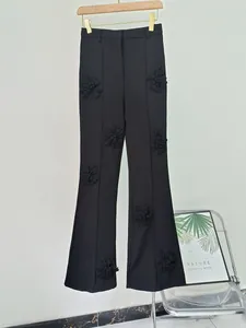 Primo piano di pantaloni neri a zampa con eleganti applicazioni di fiori in tessuto 3D.
