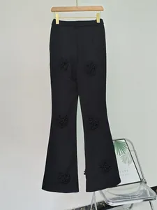 Dettaglio che mostra le eleganti decorazioni floreali in tessuto 3D su pantaloni neri svasati.