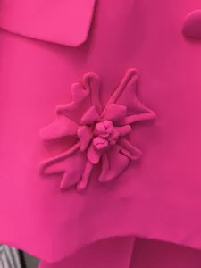 Dettaglio ravvicinato dell'elegante fiore 3D in tessuto su blazer rosa stile francese.