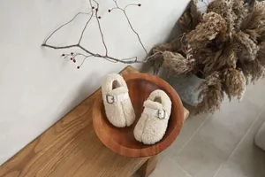 Detailed top view of cozy cream shearling pig-trotter baby shoes in a rustic wooden bowl