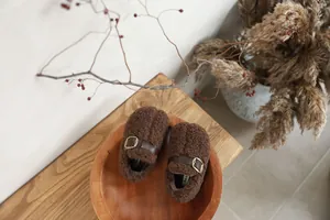 Close-up of cozy brown plush kids shoes with pig hoof design in a wooden bowl
