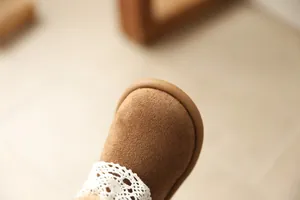 Macro detail of brown suede girls' boot with delicate white lace trim and round toe.