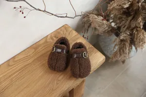 Detailed view of brown plush children's shoes with leather buckle and warm lining.