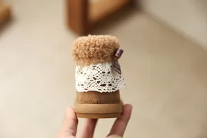 Detail of girl's brown fleece boot with lace trim and small plaid bow decoration