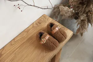 Close-up of brown fuzzy fleece children's slip-on shoes with leather buckle strap