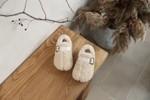 Detailed view of plush cream children's slip-on loafers with buckle strap on wood