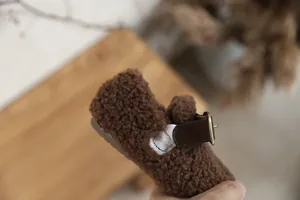 Close-up of brown fleece children's shoe featuring a leather strap and gold buckle