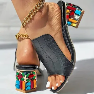 Close-up detail van zwarte sandalen met krokodillenmotief en kleurrijke strasblokhakken.