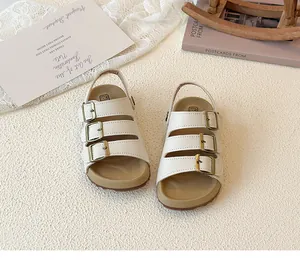Detailed view of children's white triple-strap sandals with cork sole and bronze buckles.