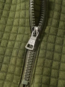 Detailaufnahme eines silbernen Metallreißverschlusses an olivgrünem Waffelstrick-Sweatshirt