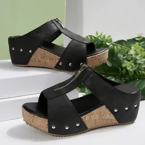 Detail view of black wedge sandals with front zipper and decorative silver studs.