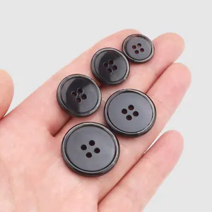 Assorted sizes of dark brown urea garment buttons with four holes held in a hand