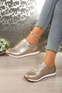 Λεπτομερής λήψη μεταλλικών χρυσών sneakers με κορδόνια και λευκή σόλα.
