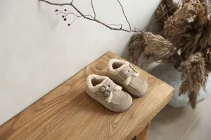 Vue détaillée de chaussures chaudes pour enfants fourrées beige sur un banc en bois.