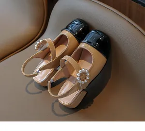 Primo piano di sandali per bambini in vernice beige e nera con fibbia di perle.