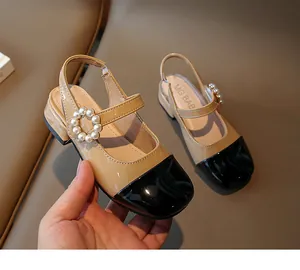 Dettaglio di sandali in vernice beige e nero per bambine con fibbia di perle.