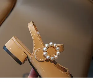 Dettaglio di sandali in vernice beige per bambine con elegante fibbia decorata di perle.