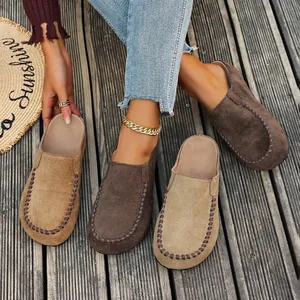Detail of women's vintage suede mules with decorative whipstitch on a wooden deck.