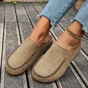 Detailed view of khaki suede closed-toe mules with whipstitched edges on wooden deck