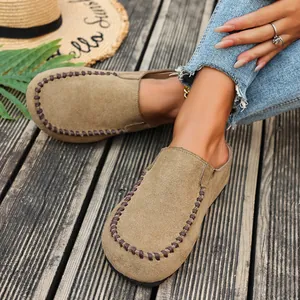 Close-up of khaki suede closed-toe mules with hand-stitched details on wooden deck