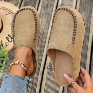 Close-up of tan suede platform clogs with decorative stitching and wood background