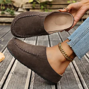 Detailed view of brown suede closed-toe mules with thick soles on a wooden deck background