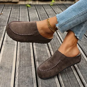 Detailed view of brown suede platform mules featuring retro stitched edges on wooden deck