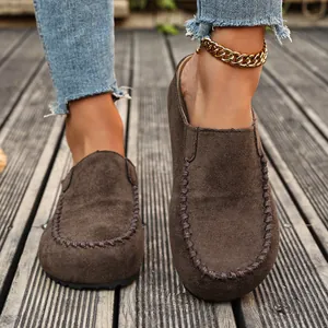 Close-up view of brown suede platform clogs with decorative stitching on a wooden deck.