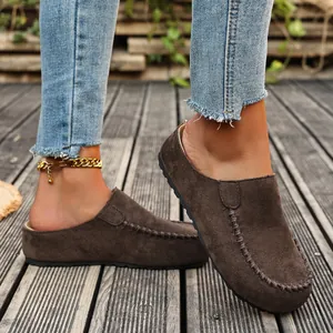 Detail shot of dark brown suede closed-toe mules worn with denim jeans on wood deck