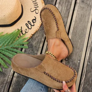 Close-up detail of brown suede platform clogs with decorative hand-stitching on a wooden background