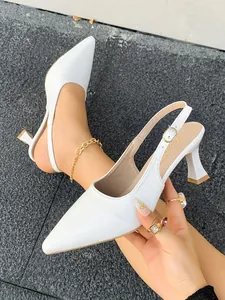 Gros plan sur d'élégants escarpins slingback blancs à bout pointu avec boucle dorée sophistiquée.
