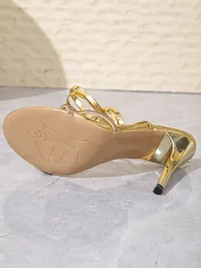 Unteransicht der goldenen Stöckelsandalette mit Gummisohle und Strass-Details