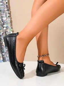 Close-up of black woven ballet flats with bow detail worn on a model's feet in studio