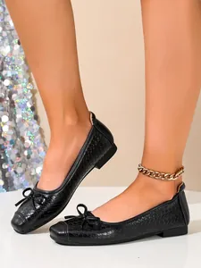 Side detail of black woven ballet flats with elegant bow decoration and flat soles.