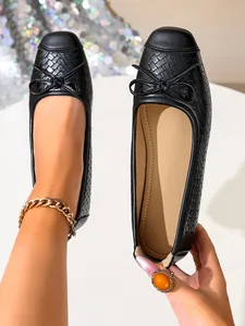 Close-up detail of black French style ballet flats with woven texture and bow detail